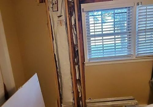 Partially demolished interior wall beside a window with blinds in a beige room