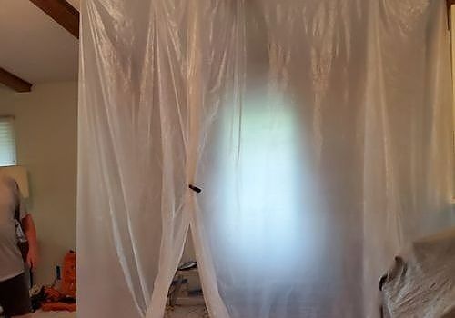 Sheer white curtains hanging in a room, with a window glowing behind them