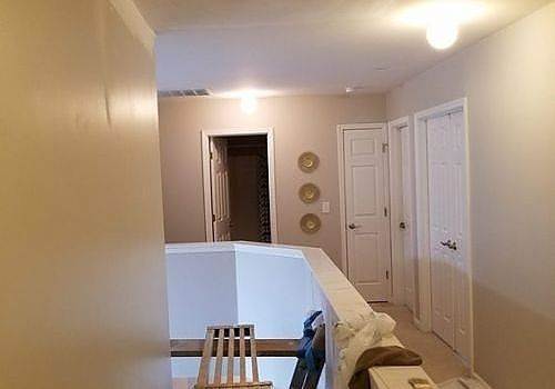 Indoor hallway with beige walls, white railing, closed doors, and framed wall decor near a staircase.