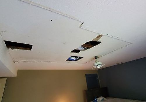 Damaged ceiling with multiple holes and missing panels in a room