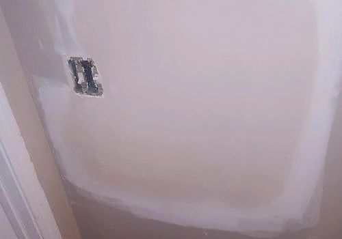 White wall or door panel with a small exposed electrical box cutout near the left side.