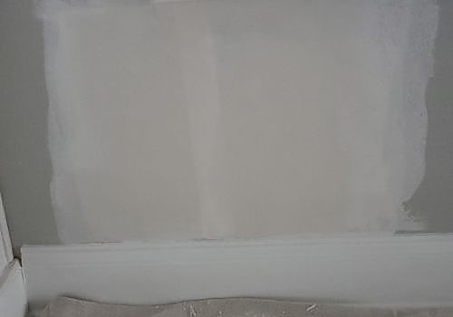 Gray primed wall section with taped edges above a white baseboard or floor trim