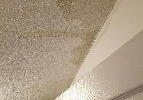 Close-up of a beige textured ceiling with a white slanted edge and water stains near the corner