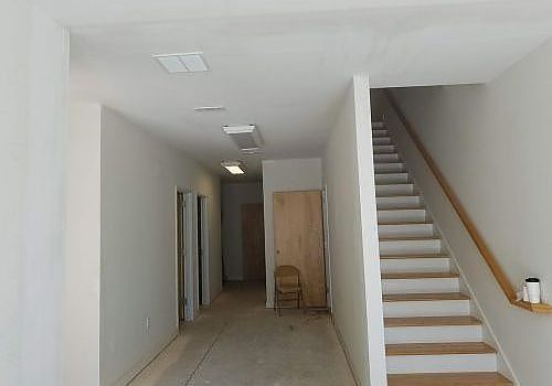 Empty interior hallway with tiled floor, staircase on the right, and a chair near a door opening.