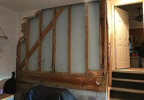 Exposed wall framing in a home interior beside a staircase and open doorway