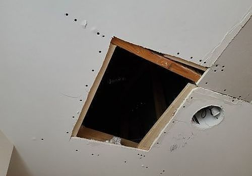 Damaged ceiling with a large square hole exposing dark attic space and a nearby recessed light opening