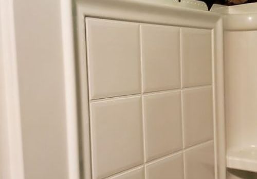 White tiled shower wall with built-in soap shelf and beige trim
