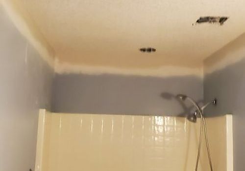 Bathroom ceiling with water damage and dark stains above a shower stall