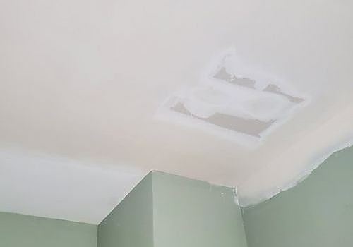 Ceiling with a large white patch of peeling paint above green walls