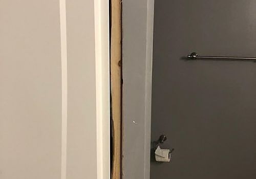 Partial view of a doorway with white trim and a gray wall-mounted shelf in a dim room