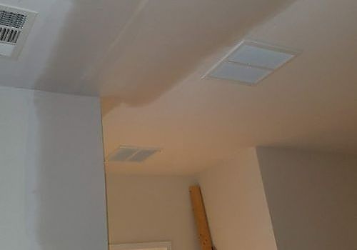 Ceiling corner with white walls, air vents, and a beige ceiling in a room.
