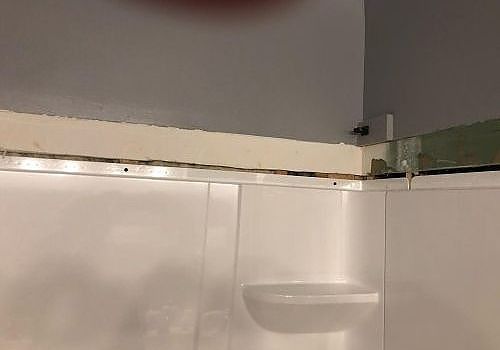 White bathroom tile wall with a small shelf and gray painted upper wall corner
