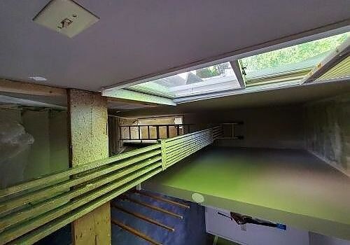 Empty indoor corridor with green railings, skylight, and blue lower walls in a worn building