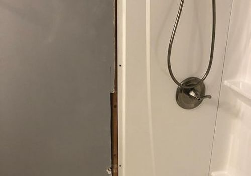 Partial view of a shower door with gray frame and silver showerhead in a white bathroom