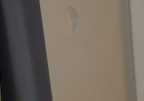 Close-up of a beige wall with a small peeled paint spot near the top center.