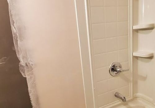 Bathtub and shower with beige tile, chrome fixtures, and a partially visible white shower curtain