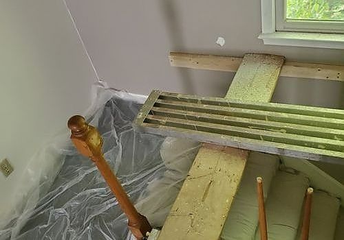 Green slatted furniture parts and wooden posts covered in plastic in a room under renovation.
