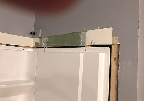 White cabinet or door under a wall opening with exposed wood trim and green insulation, in a room under construction
