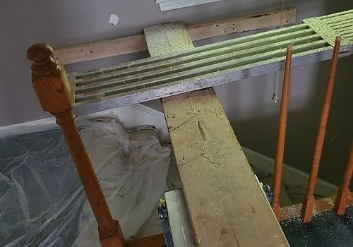 Narrow stairwell with a wooden plank bridge over a lower level, green carpet, and orange railing posts