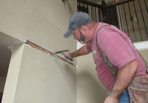 Worker sanding a wall with a long-handled tool in an indoor stairwell