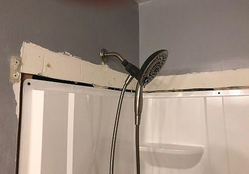 Shower head mounted on a bathroom corner near a white shower curtain.