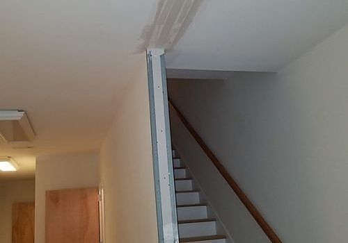 Interior stairway with white walls, gray carpeted steps, and a wooden handrail.