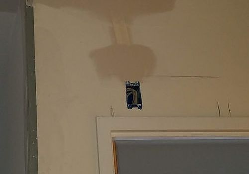 Wall above a doorway with exposed electrical wiring and a cutout outlet box.
