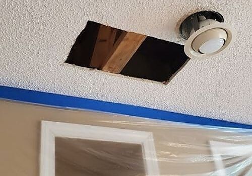 Ceiling with a damaged drywall opening, exposed wooden framing, and a recessed light fixture nearby