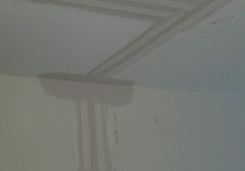 Ceiling corner with a visible water stain and peeling paint near a wall seam