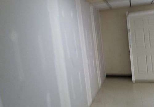 Empty hallway with white walls, tiled floor, and a partially open door on the right.