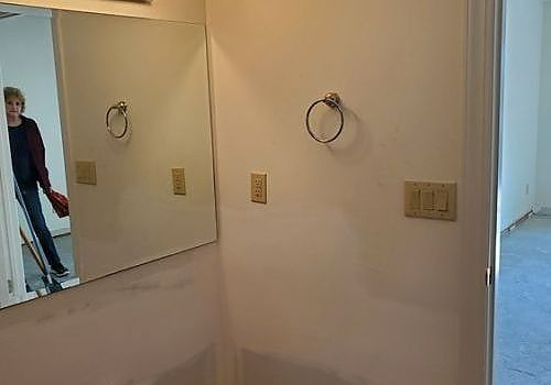 Hallway with wall mirror and two towel rings; person reflected near a doorway.