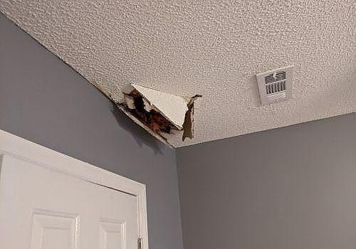 Damaged ceiling corner with a large hole above a white door in a gray room