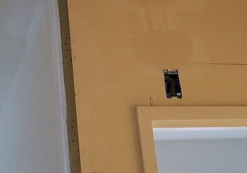 Wall with an open electrical box above a white door frame