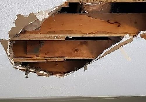 Damaged ceiling with a large hole exposing wooden beams and torn drywall