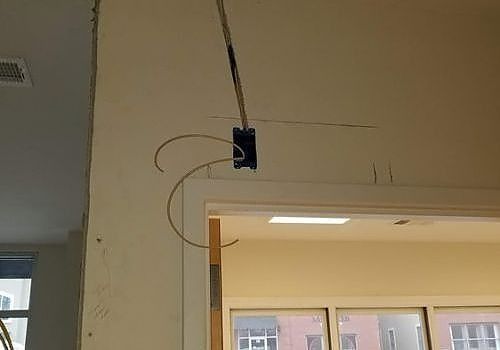 Open electrical box with loose wires above a doorway in a beige interior wall