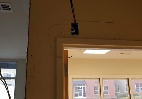 Open doorway with exposed wiring above the frame and a light fixture in a beige interior.