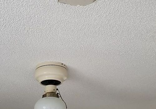Ceiling fan mount with a light bulb against a textured white ceiling