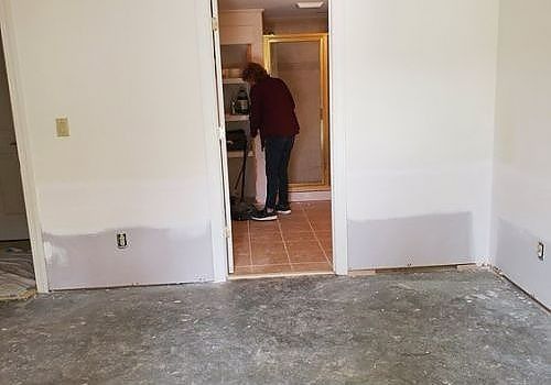 Person working in a doorway of a mostly empty room with unfinished walls and floor