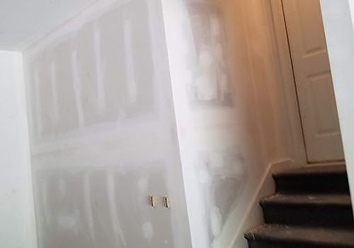 Drywalled hallway with a staircase and cabinet, white walls, and wood trim.