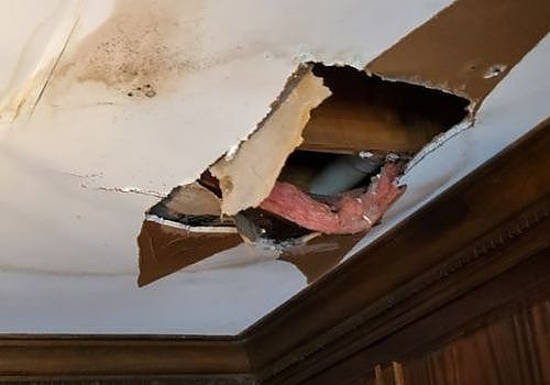 Damaged ceiling with a large hole exposing insulation and framing