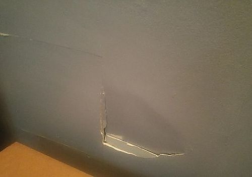 Close-up of a gray wall with a small crack and chipped paint near the bottom edge.