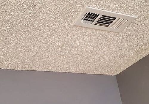 Ceiling air vent on a textured white ceiling above gray walls