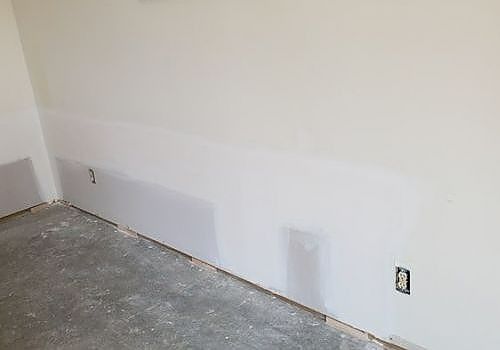 Empty white room corner with bare concrete floor and electrical outlets on the wall