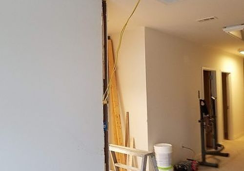 Partially renovated hallway with exposed framing, tools, and a chair against beige walls