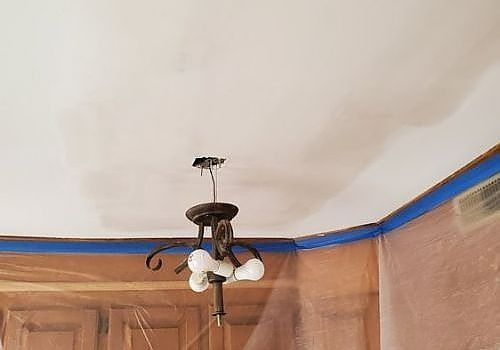 Ceiling light fixture with exposed wires in a room corner, under a white ceiling and blue trim