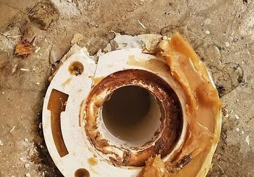 Rusty circular metal pipe opening set in dirt, surrounded by white plastic and debris