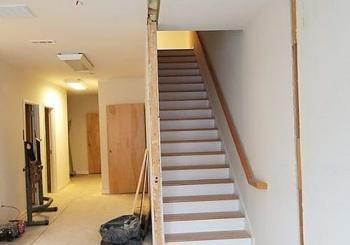 Interior hallway with unfinished stairs leading up, white walls, wooden handrail, and construction materials on the floor