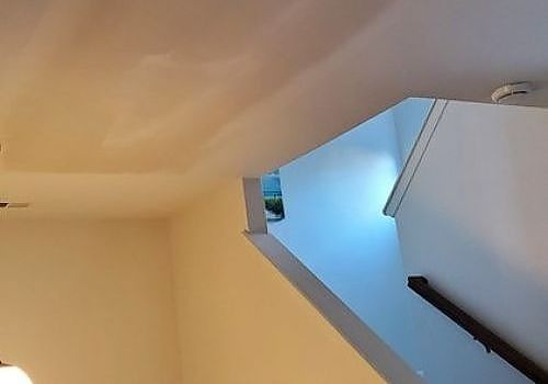 Indoor stairwell with cream walls, blue-lit landing, and a black handrail view from below