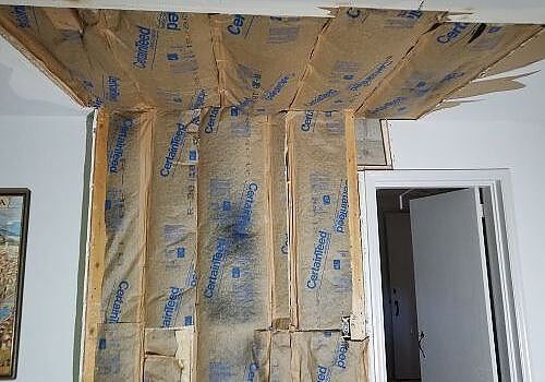 Room under construction with insulation exposed around a ceiling beam and doorway.