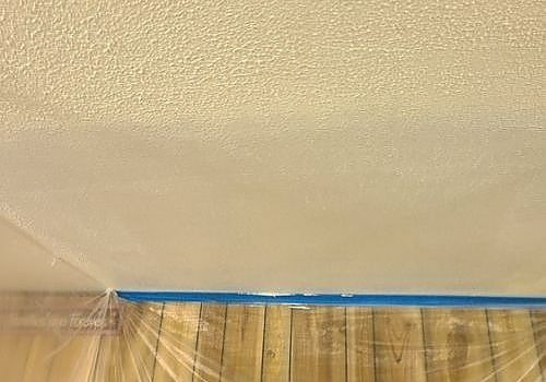 Ceiling corner with textured beige paint and a blue tape line above tan curtains